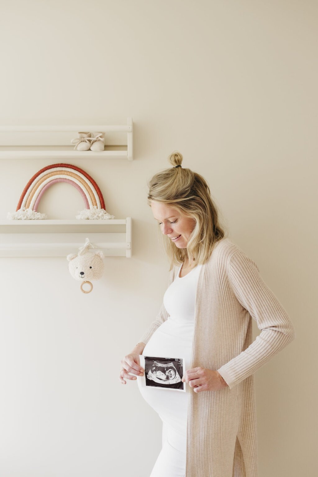 Zwanger in babykamertje met echo foto bij zwangere buik voor Naviva Kraamzorg.